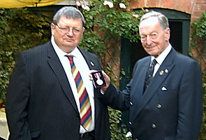 Tony (left) receiving his medal from Sir Stephen Brown GBE (right).